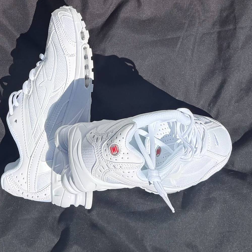 All white Nike Shox Ride 2 sneakers, one propped against the other on a dark cloth